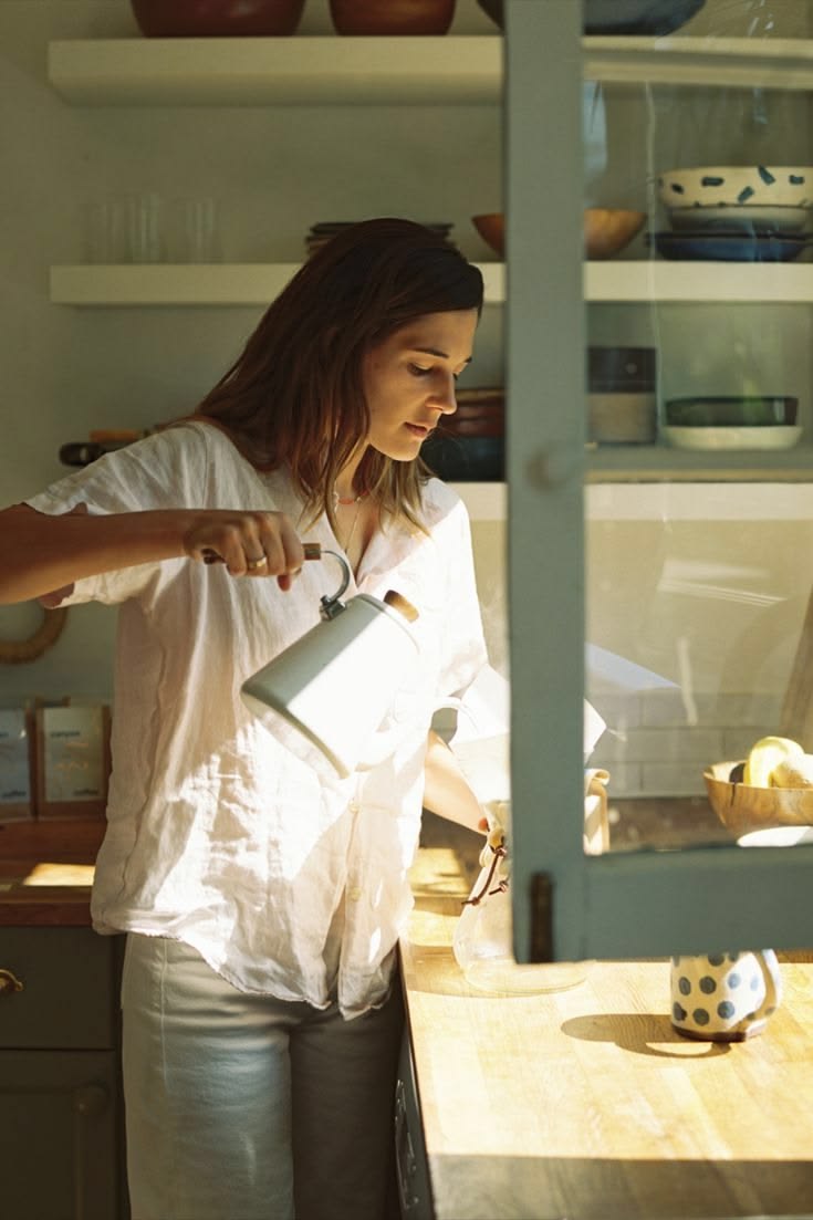 a women standing in the kitchen making her morning coffee